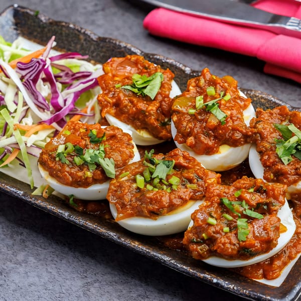 Indian deviled eggs, topped with a rich, spicy red sauce and fresh herbs, served with shredded cabbage.