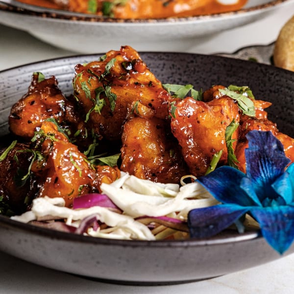 Kashan Indian Kitchen & Bar's chicken dish, garnished with fresh herbs and a blue orchid.