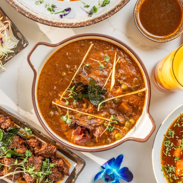 Overhead view of various Indian dishes, including a rich brown curry, a meat dish, and drinks.