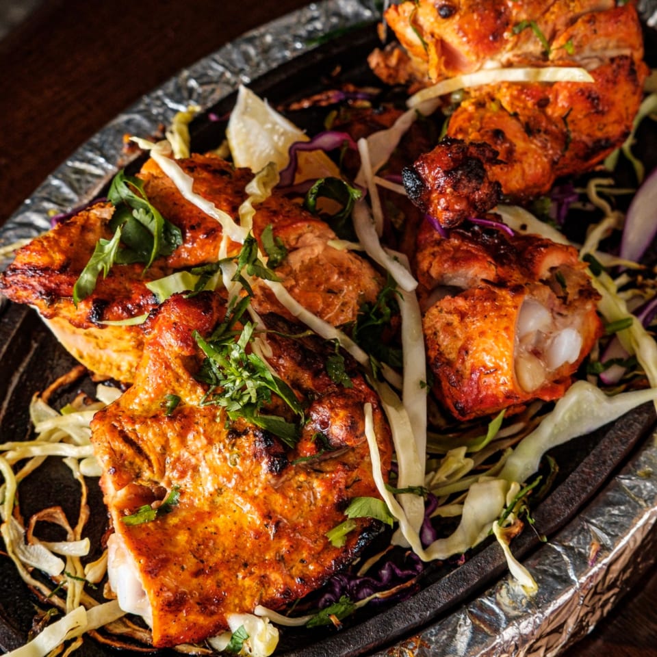 Kashan Indian Kitchen's Tandoori Chicken, garnished with cabbage, cilantro, and lemon, served on a hot platter.