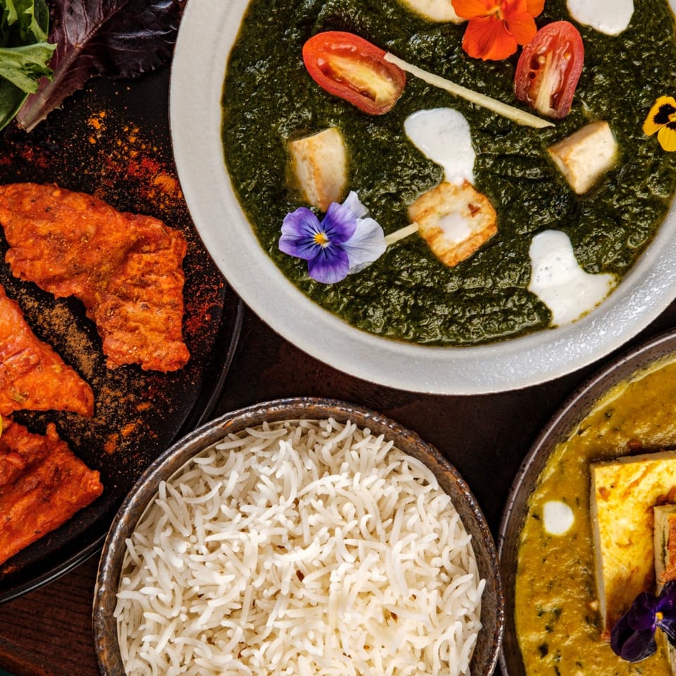 Overhead view of Indian dishes: palak paneer, chicken tikka, rice, and another paneer curry.