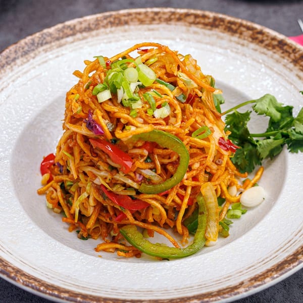 A vibrant Indian noodle dish with bell peppers, green onions, and cilantro on a white plate.
