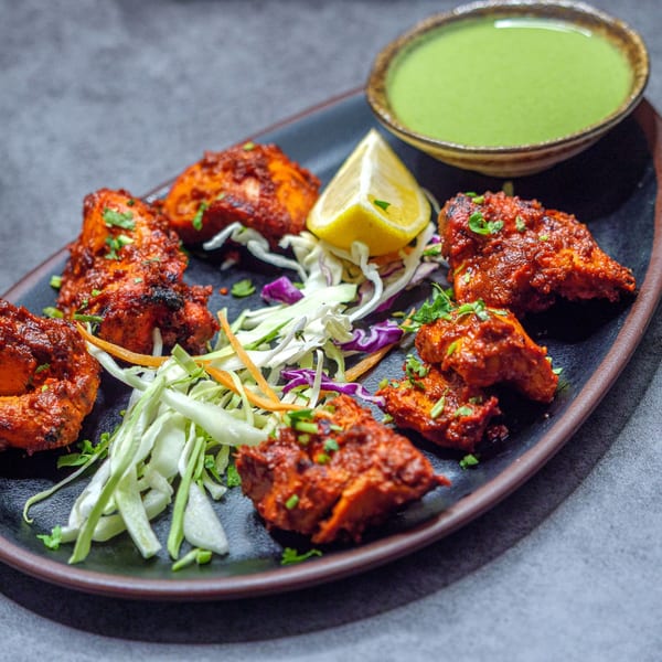 Kashan Indian Kitchen's chicken tikka, garnished with cilantro, lemon, and shredded cabbage, with green chutney.