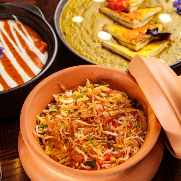 Indian biryani in a clay pot, with two other Indian dishes in the background.